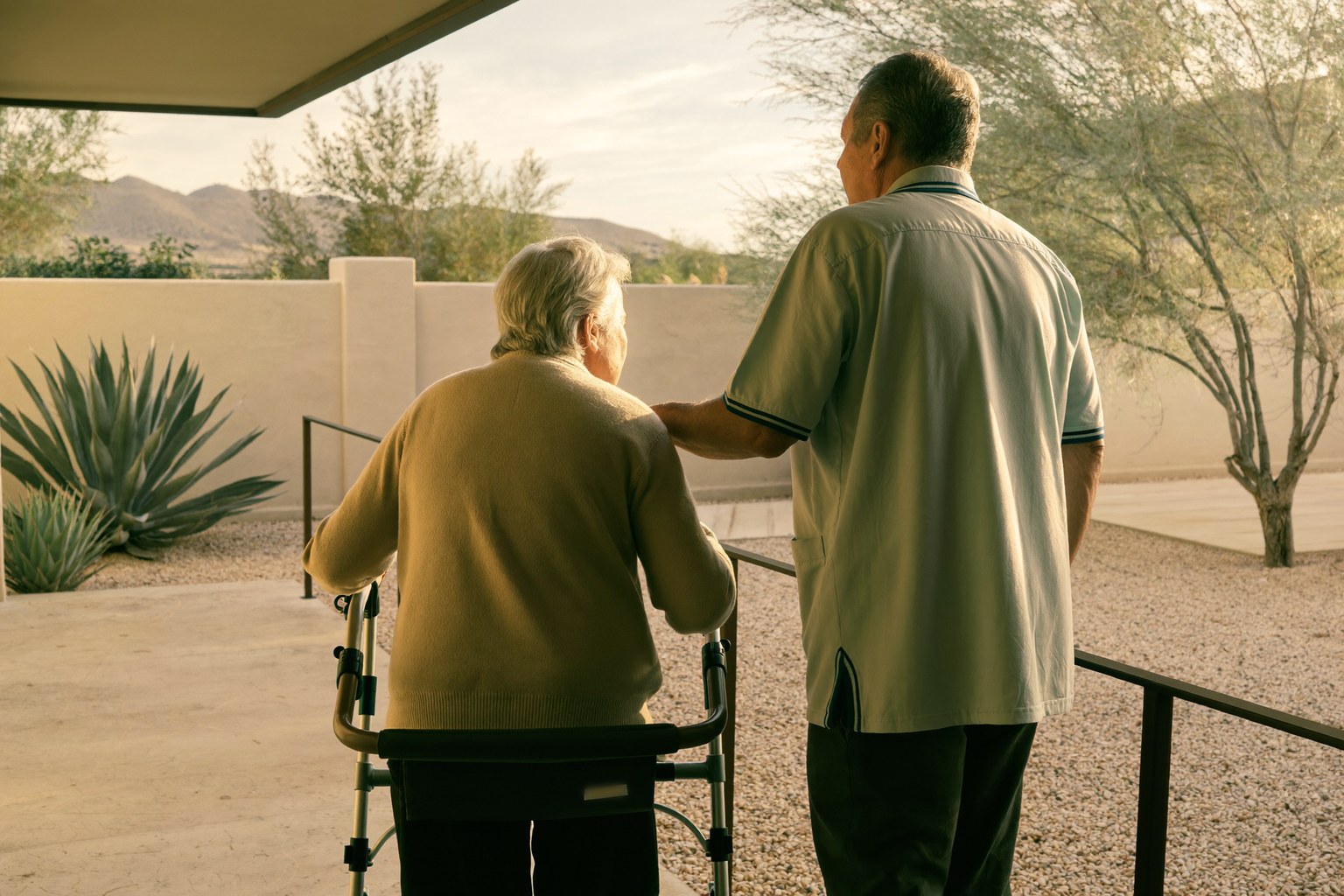Caregiver walking beside an older woman using a walker on a backyard patio